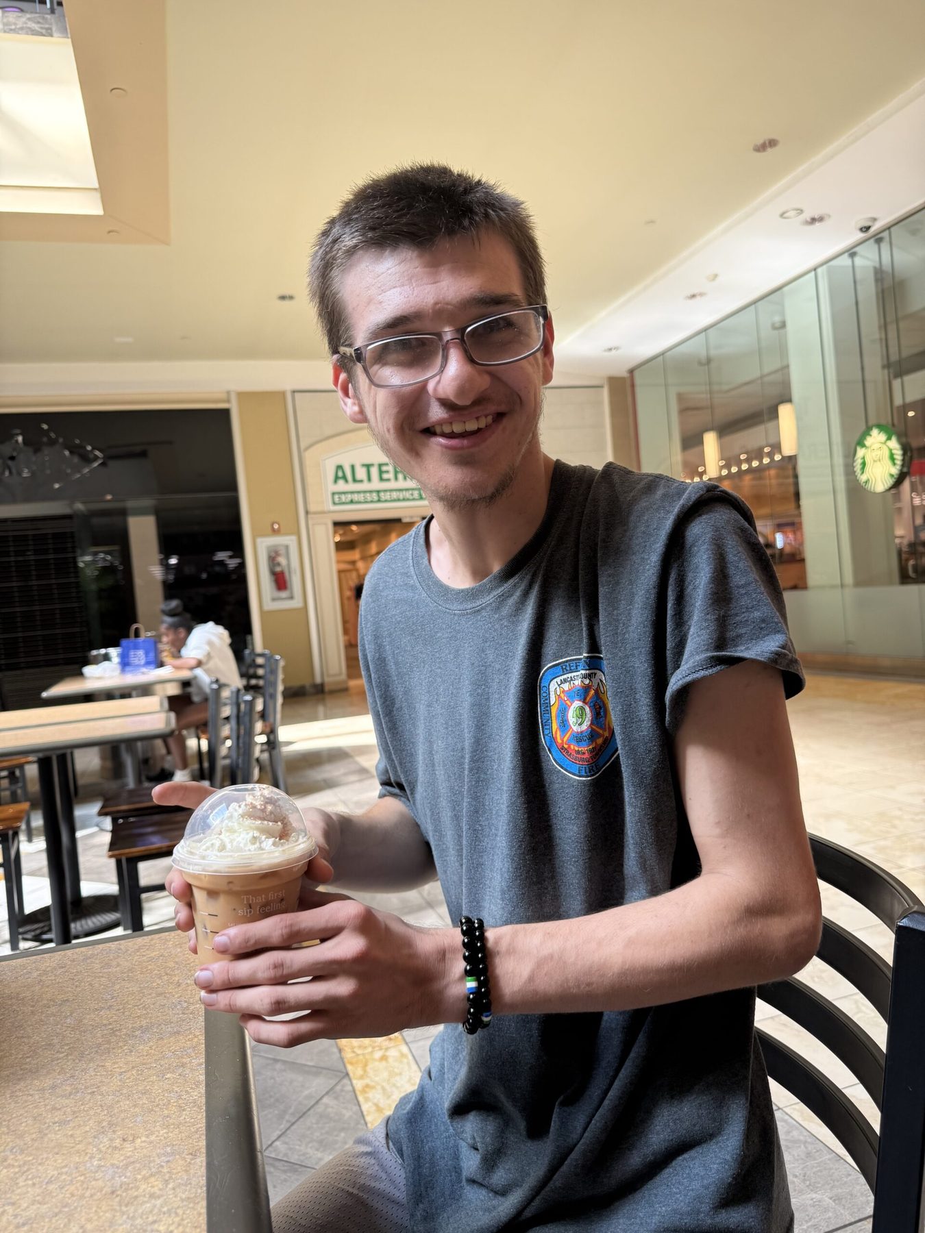 A young man smiling over a drink at a café