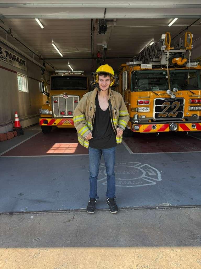 A young man in a firefighter helmet and jacket at a fire station