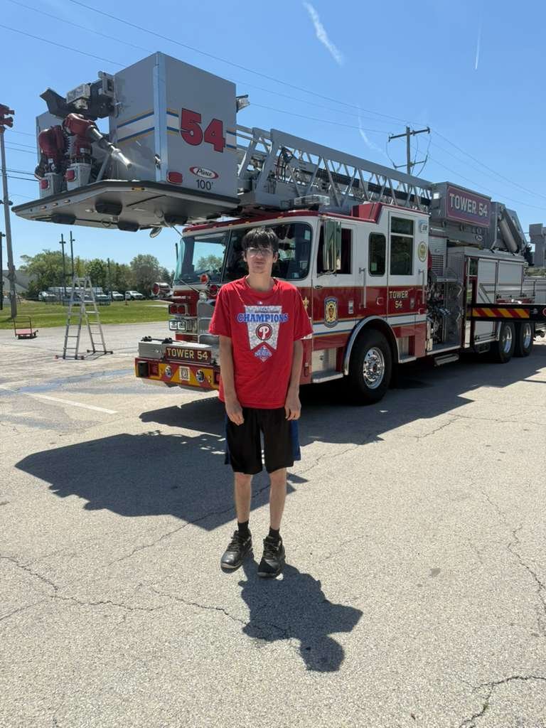 A young man standing in front of a fire engine on a sunny day