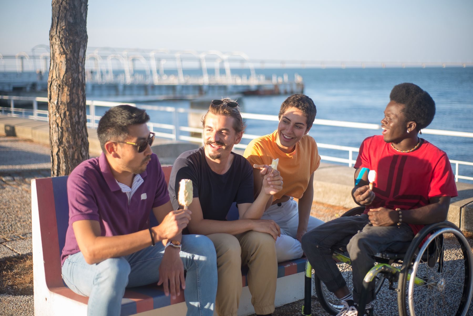 Friends sharing ice cream on a bench by the water